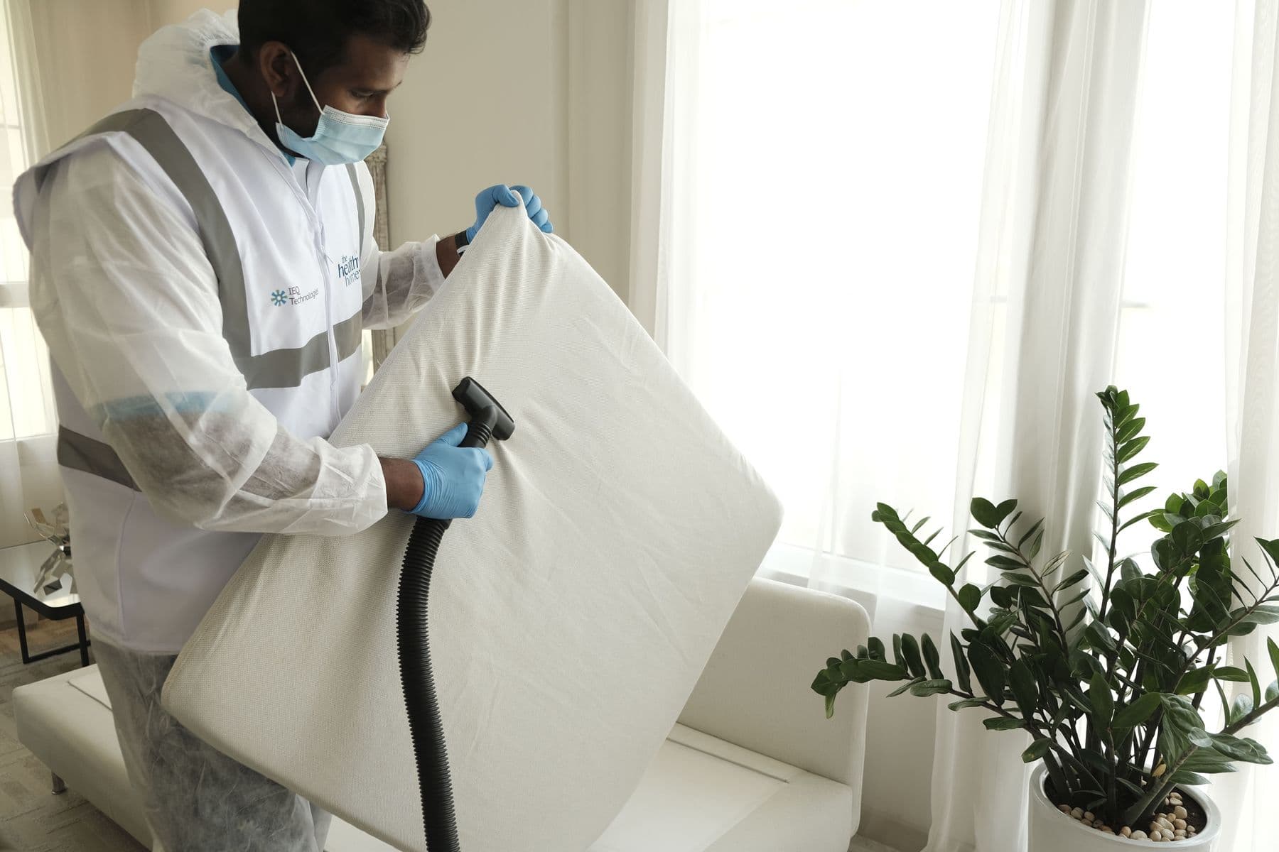 Technicien en tenue de protection nettoyant un matelas à domicile avec un injecteur-extracteur